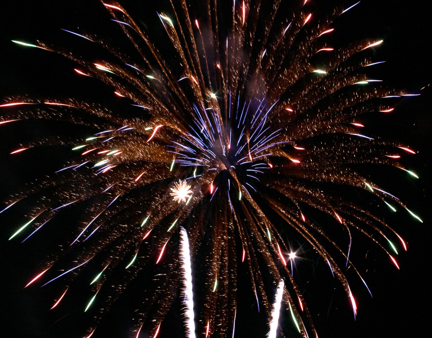 A dramatic Bonfire Night scene with fireworks exploding above a glowing bonfire and crowd