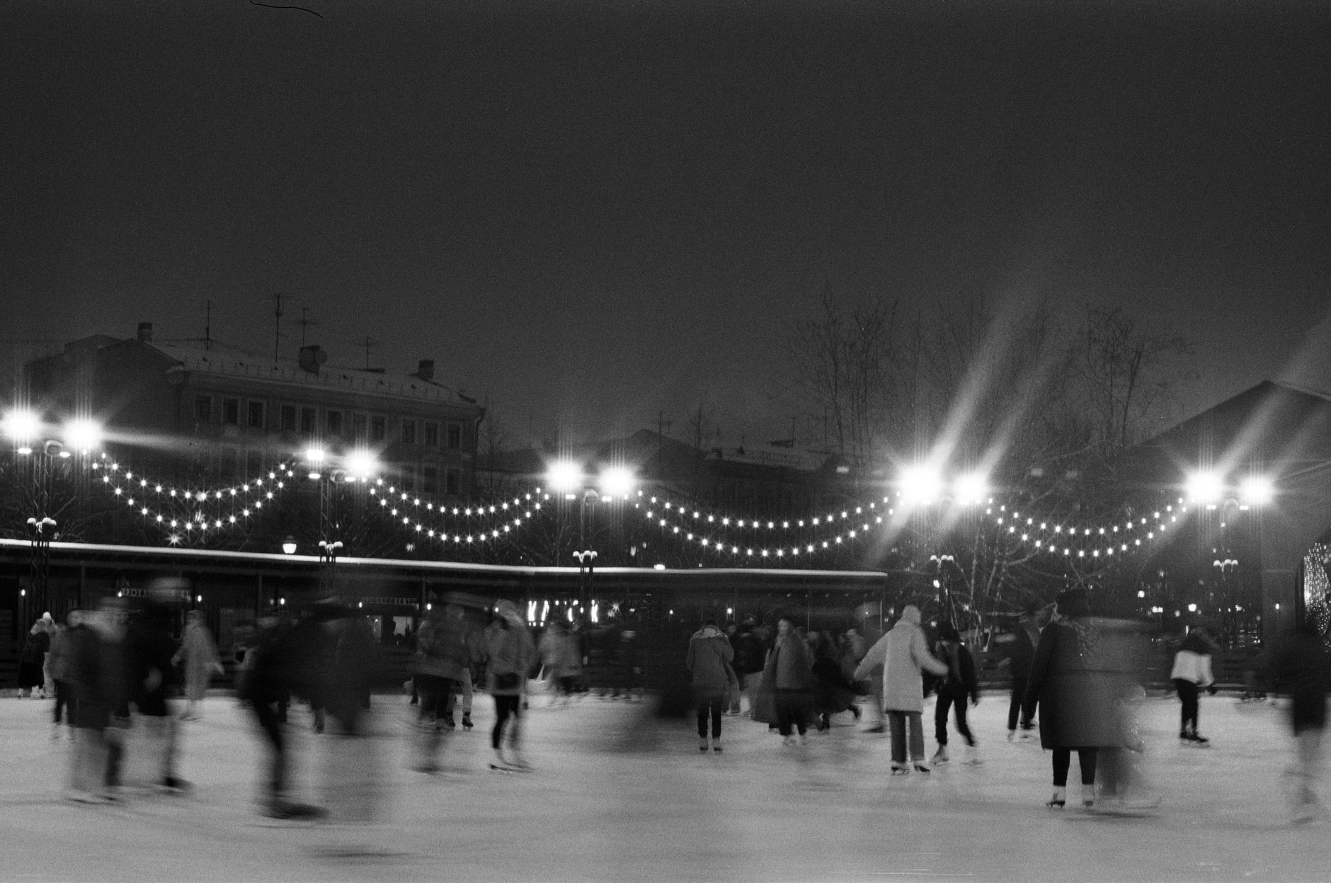 People ice skating on an outdoor rink surrounded by festive lights on a winter night